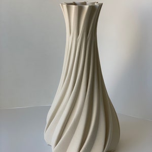 May include: A tall, cream-colored vase with a unique, textured design. The vase features a spiraling, ribbed pattern that flows from the base to the ruffled top. The neutral color and elegant shape make it a versatile decorative piece.