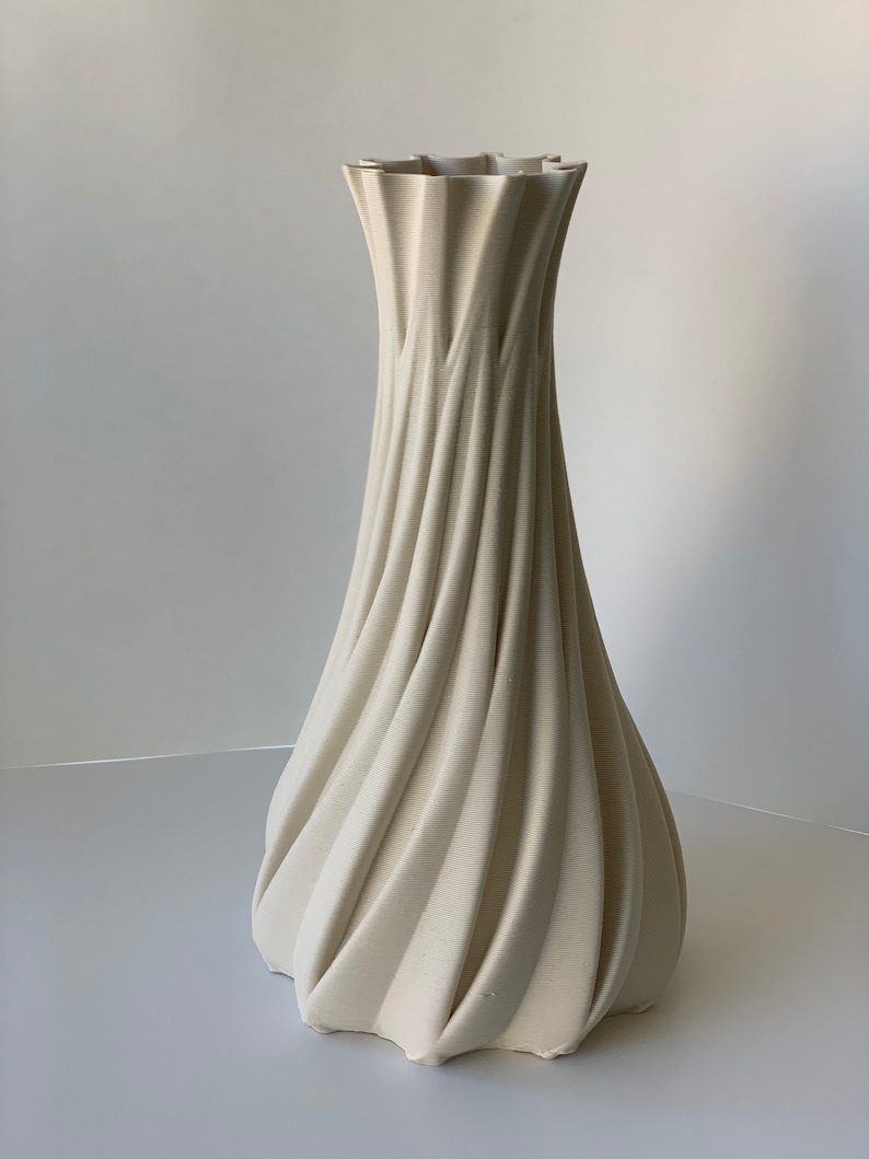 May include: A tall, cream-colored vase with a unique, textured design. The vase features a spiraling, ribbed pattern that flows from the base to the ruffled top. The neutral color and elegant shape make it a versatile decorative piece.