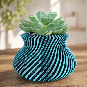 Puede incluir: Una maceta a rayas turquesa y negras que contiene una planta suculenta verde. La maceta tiene un diseño ondulado único con rayas verticales. La planta tiene múltiples hojas verdes. La maceta está sobre una superficie de madera.