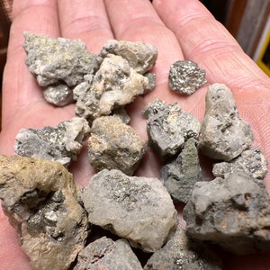 May include: A handful of raw pyrite and quartz mineral specimens. The rough, irregular stones display a mix of gray, tan, and metallic gold colors. The pyrite crystals glisten, contrasting with the matte quartz.