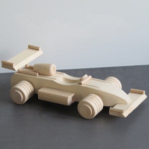Könnte beinhalten: Ein hölzernes Spielzeug-Rennwagen mit Spoiler, Rädern und einem detaillierten Motor. Das Auto ist aus Naturholz gefertigt und unbemalt.