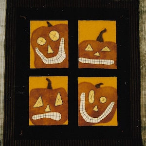 May include: Four felt pumpkin faces with different expressions, stitched in brown and white thread on a brown background. The pumpkins are orange with a yellow background.