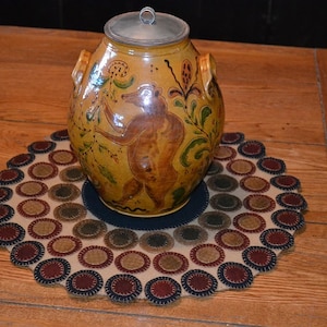 May include: A yellow ceramic jar with a brown bear and floral designs sits on a round, cream-colored rug with brown, blue, and red circles.