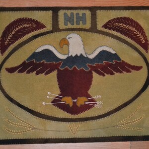 May include: A brown and tan felt wall hanging with an embroidered bald eagle, wheat stalks, and the letters "NH".