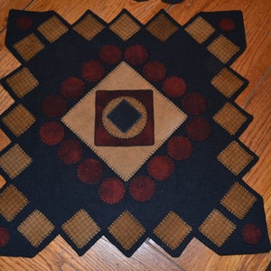 May include: A black wool rug with a geometric design featuring brown and red squares and circles. The rug has a diamond shape and is made with a patchwork technique.