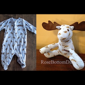 May include: A light blue baby sleeper with a brown moose pattern and a matching moose plush toy. The sleeper has a snap closure and the text "Salt Lake Goods" on a label. The plush toy has large brown antlers.