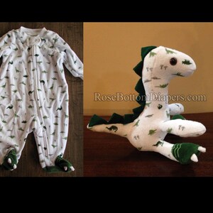 May include: White baby sleeper and stuffed dinosaur toy, both featuring a green dinosaur pattern. The sleeper has a full-length zipper and footed design. The plush dinosaur has green accents and large, round eyes.
