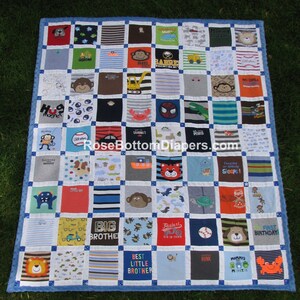 May include: A handmade quilt made from various children's t-shirts, featuring colorful designs and text. The quilt has a blue border and is laid out on green grass. The t-shirts have images of animals, vehicles, and phrases like "Best Little Brother."