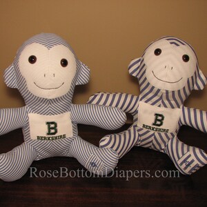 May include: Two plush monkey dolls. Each monkey has a white face and ears, brown eyes, and a stitched smile. The bodies are blue and white striped fabric. Each monkey has a white patch with a green "B" and the word "Berkshire".