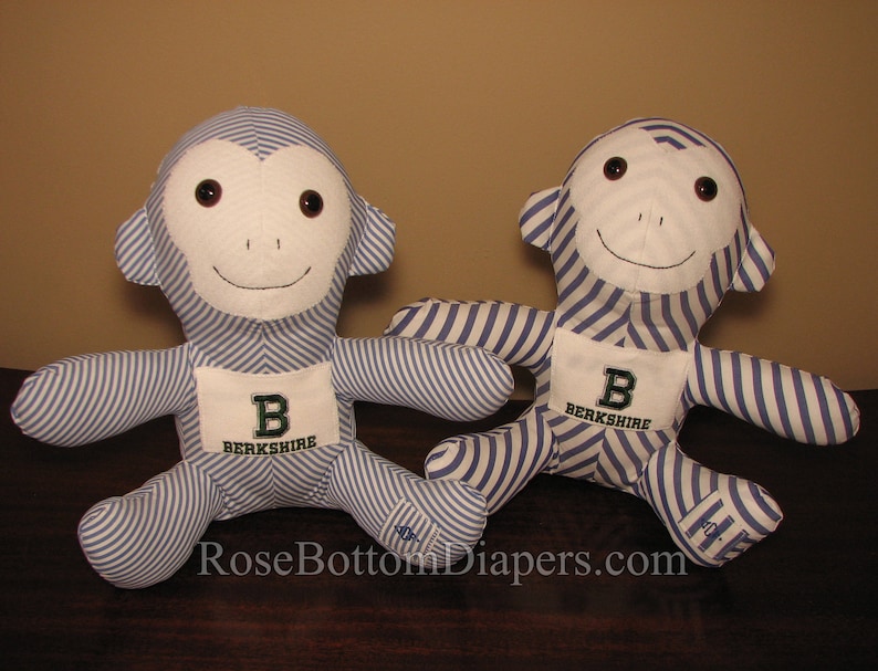 May include: Two plush monkey dolls. Each monkey has a white face and ears, brown eyes, and a stitched smile. The bodies are blue and white striped fabric. Each monkey has a white patch with a green "B" and the word "Berkshire".