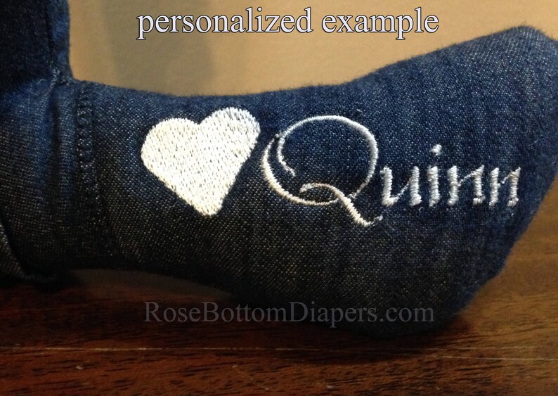 May include: Close-up of a denim fabric item with white embroidered details. A white heart is embroidered next to the name "Quinn" in white script. The text "personalized example" is at the top.