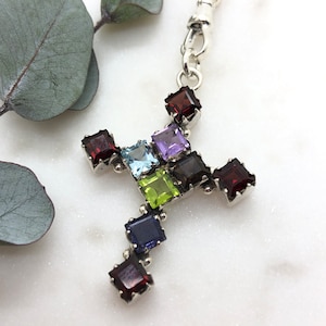 May include: A silver chain necklace with a silver cross pendant featuring a variety of colourful gemstones, including red, blue, green, purple, and brown.