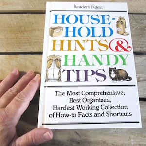 May include: A Reader's Digest book titled "Household Hints & Handy Tips." The cover features the title in various colors, illustrations of a file folder, a jar, a window with curtains, and a cat. The book promises a comprehensive collection of facts and shortcuts.