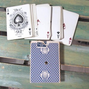 Puede incluir: Una baraja de cartas con un patr&oacute;n de diamantes azules y blancos en el reverso. Las cartas est&aacute;n abanicadas, mostrando el As de Picas con "BEE" y "CONSOLIDATED-DOUGHERTY" impresos. La baraja est&aacute; etiquetada como "Atlantis".