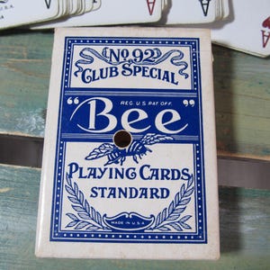 Puede incluir: Una baraja de cartas vintage "Bee Playing Cards Standard" en una caja blanca y azul. La caja presenta el texto "No. 92 Club Special" y una ilustraci&oacute;n de abeja. La baraja est&aacute; hecha en los EE. UU.