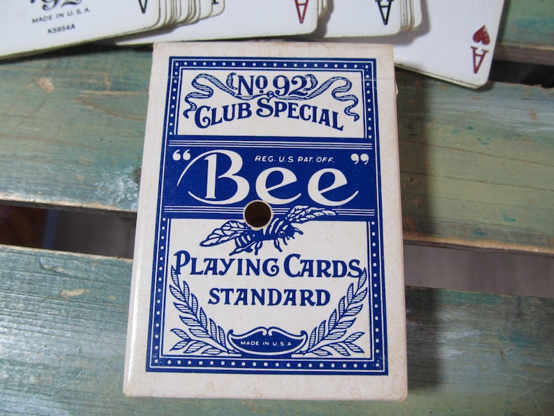 Puede incluir: Una baraja de cartas vintage "Bee Playing Cards Standard" en una caja blanca y azul. La caja presenta el texto "No. 92 Club Special" y una ilustraci&oacute;n de abeja. La baraja est&aacute; hecha en los EE. UU.