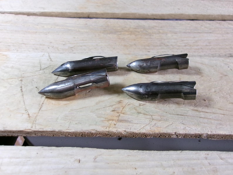 May include: Four vintage metal arrowheads with a silver finish are arranged on a light-colored wooden surface. Each arrowhead has a pointed tip and a small fin-like structure at the back. The arrowheads are likely for hunting or display.