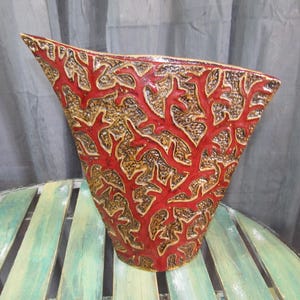 May include: Red ceramic vase with a textured coral design. The vase is shaped like a wide, shallow bowl with a pointed spout.