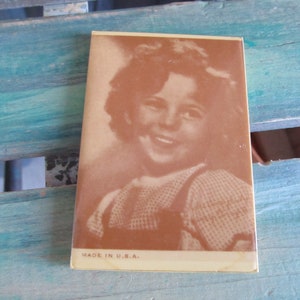 May include: A vintage sepia-toned photograph of a young girl with curly hair smiling. The photo is printed on a cream-colored card with the text "MADE IN U.S.A." at the bottom.