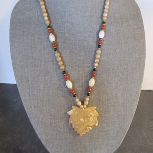 May include: A beige, brown, and white beaded necklace with a large beige leaf-shaped pendant.