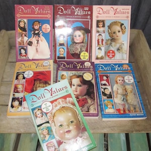 May include: A collection of nine books titled "Doll Values" with different editions and cover images featuring antique and modern dolls. The books are arranged in three rows with three books in each row.