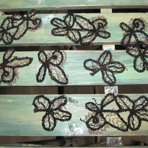 May include: Ten black and silver beaded floral appliques on a light blue wooden surface.