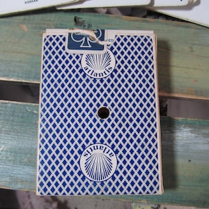 Puede incluir: Una baraja de cartas con un patr&oacute;n de diamantes azules y blancos en el reverso. La palabra "atlantis" est&aacute; impresa en el reverso de la baraja en un dise&ntilde;o circular. La baraja tiene un agujero en el centro.