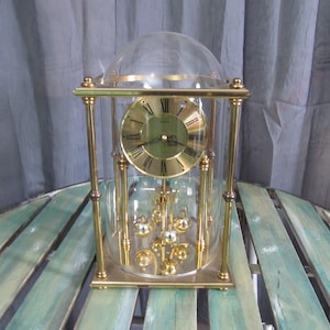 May include: A gold-toned mantel clock with a glass dome and a pendulum. The clock face has Roman numerals and black hands.
