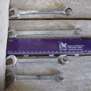 May include: Four silver wrenches of different sizes, with the measurements 7/16, 1/2, and 1/8 printed on them. The wrenches are laid out on a wooden surface with a purple ruler.