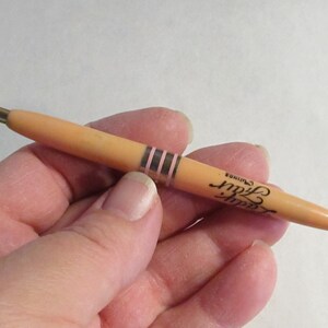 May include: A peach-colored pen with gold accents and the text "Lady Fair" in black script. The pen has a gold tip and a decorative band with pink stripes. A classic writing instrument.