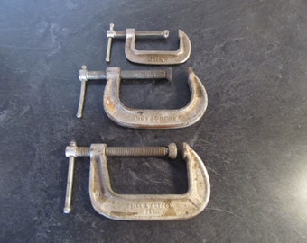 May include: Three metal C-clamps of different sizes. The largest clamp is labeled "JUNK & COTTON PAT", the middle clamp is labeled "DEVILBISS", and the smallest clamp is labeled "SHO".