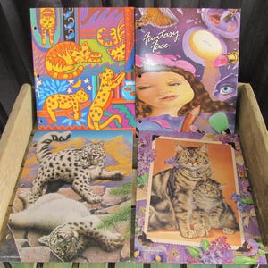 May include: Four different vintage school binder covers featuring colorful illustrations of cats. The covers include a colorful abstract design with cats, a snow leopard, a tabby cat and kitten, and a woman with makeup and the text "Fantasy Face".