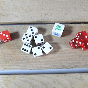 May include: A collection of dice in various colors and arrangements. Several white dice with black dots are scattered, along with red dice. One die has the words "Go Free" printed on it.