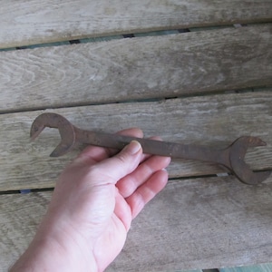 May include: A rusty wrench with a single open end and a closed end. The wrench is held in a hand.
