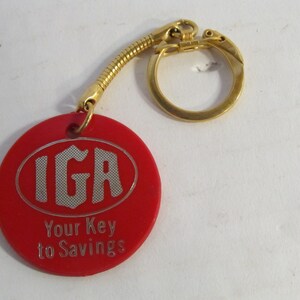 May include: Red plastic keychain with a gold metal ring and chain. The keychain has a white oval with the text "IGA" and the words "Your Key to Savings".