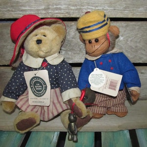 May include: Two plush toys, a bear and a monkey, dressed in red, white, and blue patriotic outfits. The bear is wearing a red hat and a blue and white dress with stars. The monkey is wearing a yellow hat with blue stripes and a blue jacket with red buttons. Both toys have tags attached.