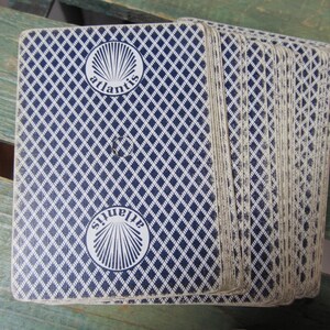 Puede incluir: Una baraja de cartas con un patr&oacute;n de diamantes azules en el reverso. Las cartas tienen la palabra "atlantis" en un c&iacute;rculo blanco. La baraja est&aacute; abanicada, mostrando los bordes de las cartas.