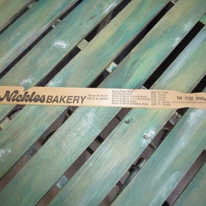 May include: A wooden oven stick with the text "Nickles Bakery" and "Brown 'N Serve Rolls & Bread" printed on it. The stick also has a baking time chart for different types of rolls, including Italian Finger Rolls, Twin French Rolls, Brown 'N Serve Oatmeal Bread, Brown 'N Serve Pull-A-Part Bread, Brown 'N Serve Rolls, and Brown 'N Serve Cinnamon Rolls. The text "The Oven Stick" is printed on the other side of the stick.
