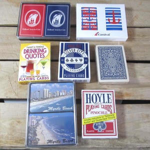 May include: A collection of playing card decks, including Holland America Line, Carnival, Silver City Standard, and Hoyle Pinochle. Some decks feature images of Myrtle Beach and drinking quotes. The decks are in various colors and designs.