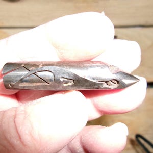May include: A vintage metal tool with a pointed end and intricate cut-out designs. The tool has a dark, aged appearance, suggesting it is antique. The design includes curved and angular shapes, and a small screw is visible near the tip.