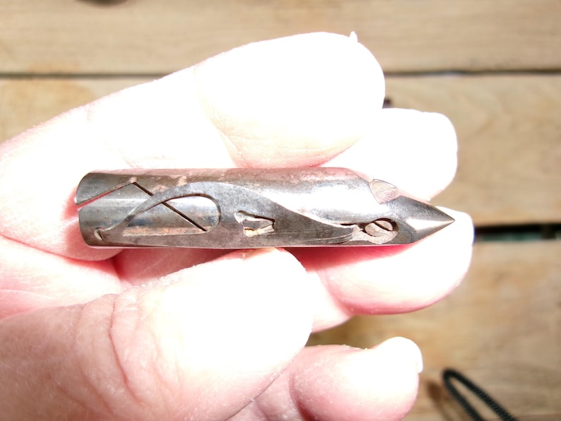 May include: A vintage metal tool with a pointed end and intricate cut-out designs. The tool has a dark, aged appearance, suggesting it is antique. The design includes curved and angular shapes, and a small screw is visible near the tip.