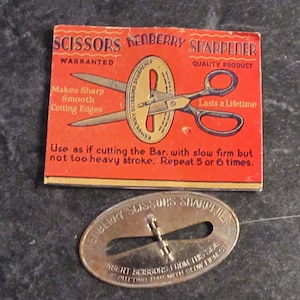May include: A vintage Kenberry Scissors Sharpener with a red and gold cardboard package. The package has the text "SCISSORS KENBERRY SHARPENER WARRANTED QUALITY PRODUCT Makes Sharp Smooth Cutting Edges Lasts a Lifetime Use as if cutting the Bar, with slow firm but not too heavy stroke. Repeat 5 or 6 times." The sharpener is a small, oval-shaped metal device with a slot for inserting scissors.