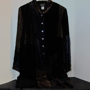 May include: A dark brown velvet jacket with a mandarin collar and button-down front. The jacket has long sleeves and two front pockets. The brand name "KOOS" is visible on the label. The jacket is displayed against a white wall.