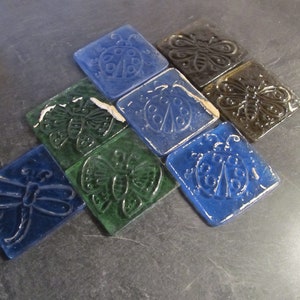 May include: Nine square glass tiles with various insect designs. The tiles are in shades of blue and green. The designs include ladybugs, butterflies, and dragonflies.