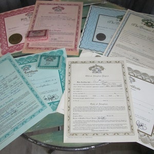 May include: A collection of eight adoption certificates from the Cabbage Patch Kids company. The certificates are printed on white paper with green, blue, and pink borders. The certificates include the name of the child, the date of birth, and the adoptive parents' names. The certificates are signed by the Cabbage Patch Kids company.