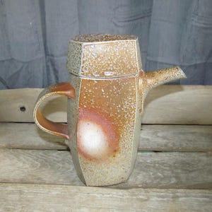 May include: A brown and white ceramic teapot with a lid and a handle. The teapot has a speckled glaze and a rounded body.