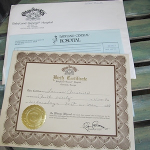 May include: A Cabbage Patch Kids birth certificate with a gold seal and the text "This certifies that  Leanne Francesca was delivered by Ruth Overly at 11:57 PM on Wednesday, 30th day of March 1988."