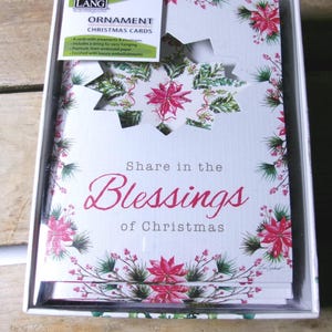 May include: A boxed set of Christmas ornament cards. The cards feature a floral design with red poinsettias and green foliage. The text "Share in the Blessings of Christmas" is displayed on the front of the cards.
