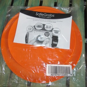 May include: Two orange silicone SafeGrabs III, a product with many uses, including a splatter guard, trivet, placement, pot grabber, funnel, utensil rest, jar opener, food cover, and much more. The product packaging includes a barcode with the number H210784143000.