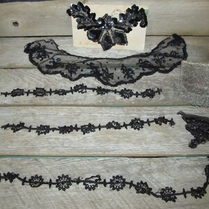 May include: A collection of black beaded lace trim and embellishments. The trim is in various lengths and styles, including a collar, a long strand, and a shorter strand. There is also a small, black beaded embellishment.